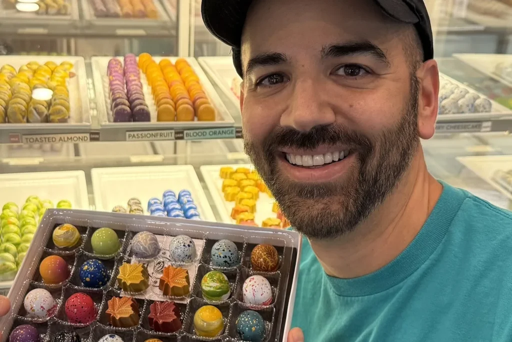A Cacao Boys founder holding a tray of hand-painted bonbons beside the shop display case