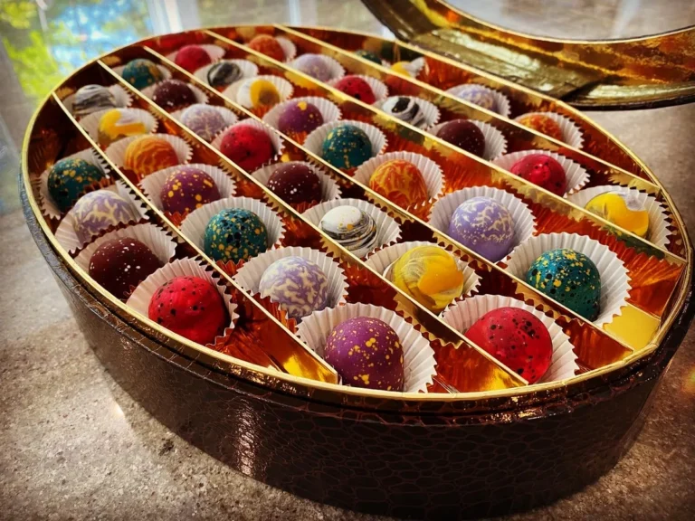 A large gold box filled with rows of colourful hand-painted bonbons