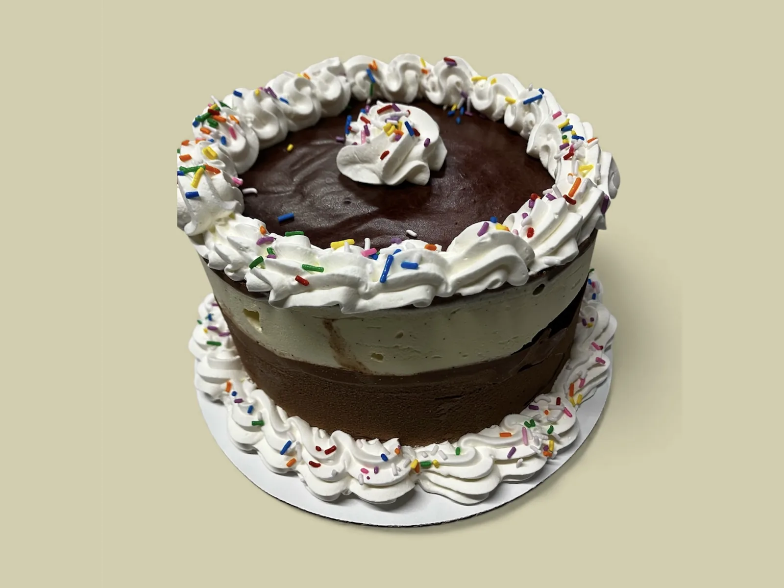 A Screamy’s ice cream layer cake, chocolate and vanilla bean layers under piped whipped cream and rainbow sprinkles